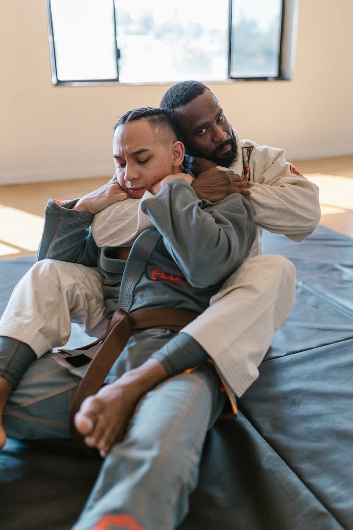 Two adult men engaged in jiu-jitsu training on indoor mats with focused expressions.